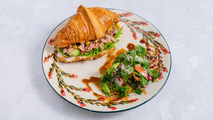 Tuna croissant sandwich and greens on paper in plate