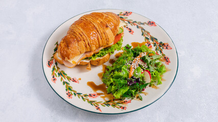 Croissant sandwich and greens on paper in plate