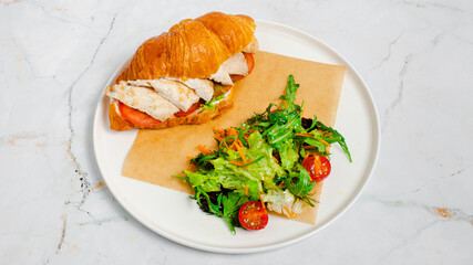 Croissant sandwich and greens on paper in plate