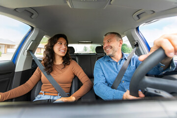 Cheerful man and woman sitting in front passengers seats in new automobile with fastening seat...