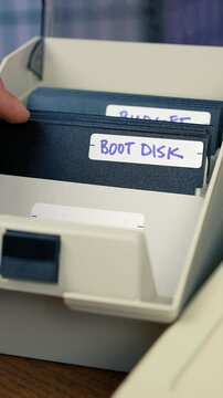 A user flips through his floppy disk caddy and locates the PORN disk. Vintage computer user concept. Vertical orientation.  	