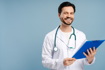 Happy smiling doctor holding clipboard on blue background looking at camera, copy space