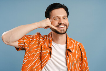 Happy, smiling man making call me gesture with hand near face standing isolated on blue background