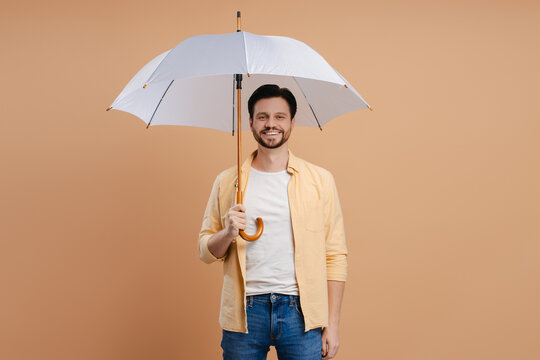 Cheerful man holding umbrella smiling at camera on beige background