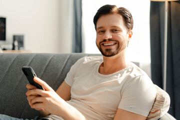 Happy man using smartphone relaxing on sofa at home