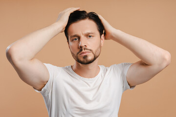 Handsome male model touching hair on beige background looking at camera hair loss problem, treatment