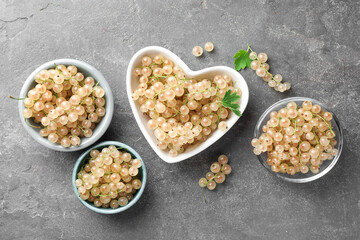 Fresh white currant berries in bowls and green leaves on gray textured table, flat lay