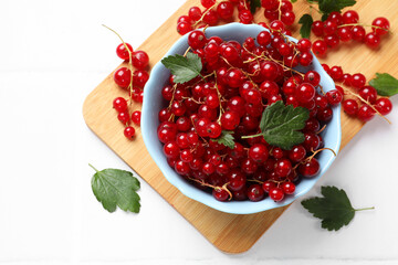 Fresh red currants in bowl and green leaves on white table, top view