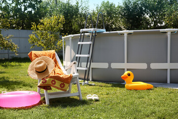 Above ground swimming pool, folding chair, towel, inflatable rings and hat in backyard