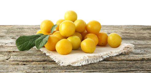 Pile of fresh plums and green leaves on wooden table against white background