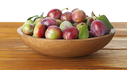 Fresh plums and green leaves in bowl on wooden table against white background