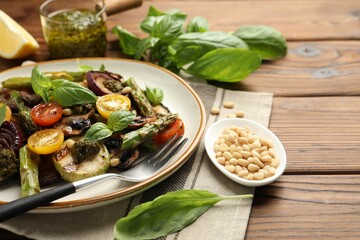 Delicious salad with grilled vegetables, basil, pine nuts and fork on wooden table, closeup