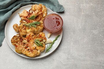 Delicious baked cauliflower steaks with sauce on grey table, top view. Space for text