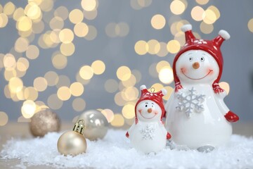 Funny snowmen figure and Christmas balls on artificial snow against blurred lights
