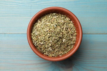 Dried oregano in bowl on light blue wooden table, top view