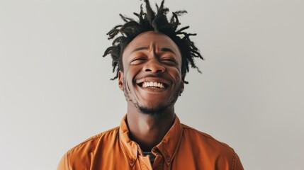 Obraz premium Portrait of a joyful young man with dreadlocks, laughing heartily while wearing a brown jacket. The bright background accentuates his expressive face, making this image perfect for themes of happiness
