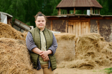 Portrait of smiling Caucasian woman with Down syndrome standing beside haystacks outdoors in rural...