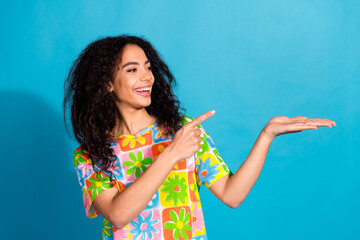 Photo of adorable lovely girl wear flower print t-shirt showing arm pointing empty space isolated blue color background