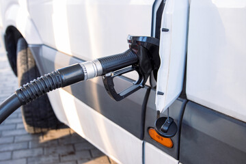 Closeup of a fuel nozzle in the car tank. Process of refilling a white transporter bus at a gas station. Refueling pistol inserted into a vehicle at a gas station. Copy space