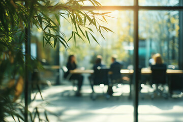 A photo looking at a blurred business meeting taking place in a glass conference room in a modern office from outside the building with sunlight coming through windows.