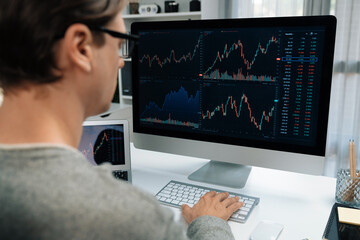 Business trader using computer and laptop to search highest profit value of dynamic increased stock market graph on working desk, analyzing exchange rate value on screen at modern office. Pecuniary.