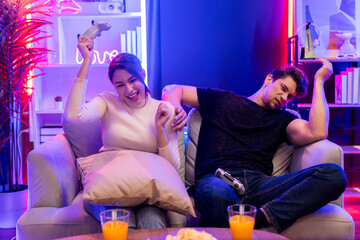 Smiling beautiful woman winner fighting gamer on video game beside loser man. Couple joyful of...