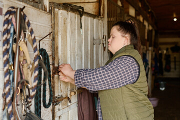 Caucasian woman locking barn door with determined expression in rustic barn setting with various equipment hanging on nearby walls capturing serene rural environment