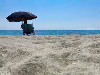 Silhouette of a man in the distance sitting alone in a sun lounger under an umbrella and enjoying the view of the sea. Low angle view