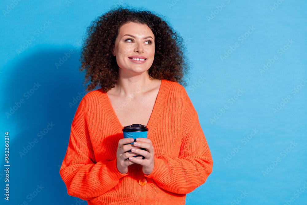 Wall mural Photo portrait of wavy haired cute latin girl wearing orange cardigan looking empty space ad new cafeteria isolated on blue color background