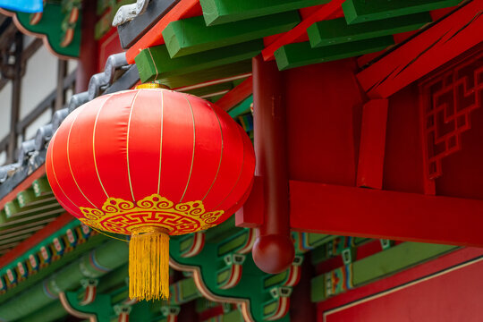 A vibrant red lantern is suspended from ornate architecture, adding color and charm to a historic area during a festival