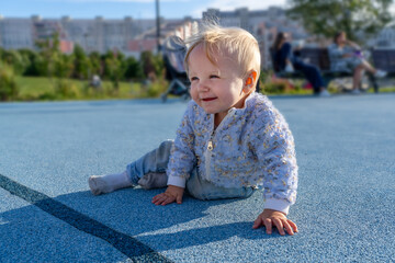 A cheerful young child sits on a bright blue surface, enjoying the warmth of a sunny day in a city park