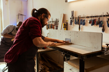Woodworking expert wears protection gear while inserting plank in spindle moulder to avoid injury. CNC machinist uses safety glasses while cutting lumber with wood shaper to prevent workplace hazards
