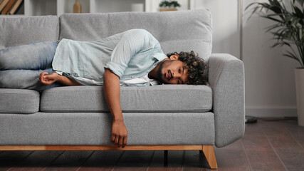 Tired Indian boy slumps on couch feeling listless. Feeling depressed, lack of motivation, sadness, boredom. Exhausted, he collapses on the couch from stress. Burn out.