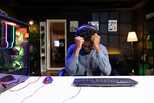 Upset gamer putting head in hands in frustration after getting game over message while playing videogame. Man feeling depressed after losing while playing on computer desktop