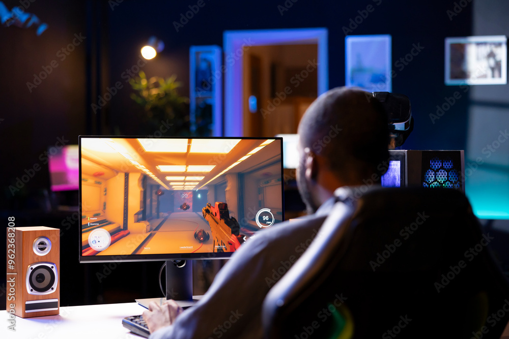 Wall mural man in living room playing video games on gaming pc at computer desk, enjoying day off from work. ga