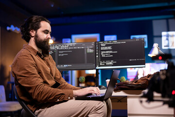 Programmer doing software debugging using laptop, checking errors in lines of code displayed on...