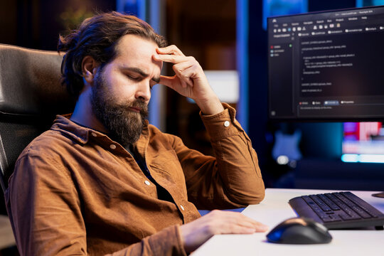 Tired man hurting from too much stress accumulated while doing software quality assurance, reading source code on computer. Developer suffers from headache after inspecting coding on PC for too long