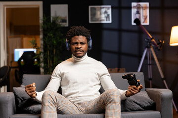 Cheerful BIPOC man playing videogames on gaming console, celebrating victory after conquering all rival players. Gamer excited after winning game, displaying happiness emotions