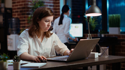 Businesswoman creating marketing project plan on laptop, writing necessary steps. Office employee...