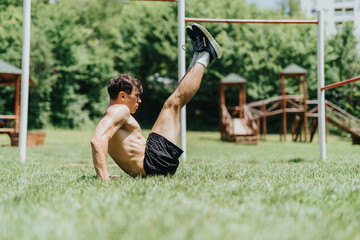Fit man exercising in nature performing leg raises in an outdoor park setting, showcasing a healthy...