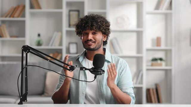 Microphone, podcast and Indian man speaker in his living room. Creative streamer, internet influencer or online content creator live streaming for audience. Camera view.