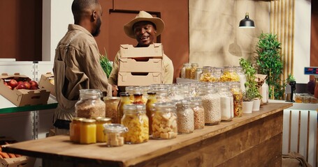 African american supplier giving fresh produce in crates to merchant, working on restocking merchandise with freshly harvested goods. Farmer and vendor collaborating on supplying store. Camera 2.