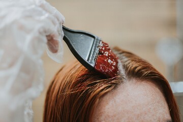 woman applying hair dye with a special brush wearing gloves at home in the bathroom