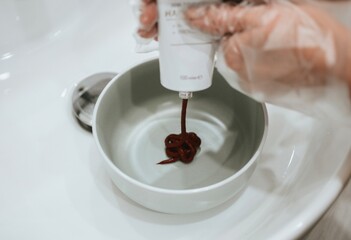 woman pours hair red dye in a bowl for dyeing red color using a special brush