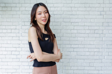 Confident Young Woman Standing with Arms Crossed Against White Brick Wall