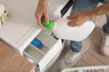 Young man pouring laundry detergent into washing machine at home, closeup