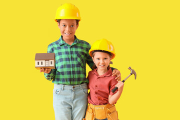 Cute little architects with house model and hammer on yellow background