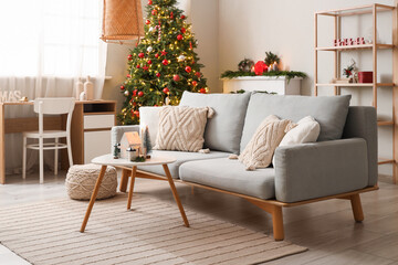 Interior of festive living room with grey sofa, coffee table and Christmas tree