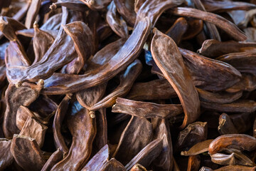 Dried carob pods. Pile of carob tree fruit pods at market stall. Top view, close-up