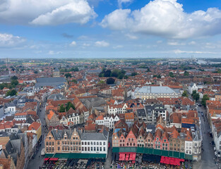 Naklejka premium Brugge, Flanders, Belgium - June 22, 2024: Sint Jacobskerk, Saint James church from Halletoren, set in urban jungle with Market square restaurant line in front under blue cloudscape